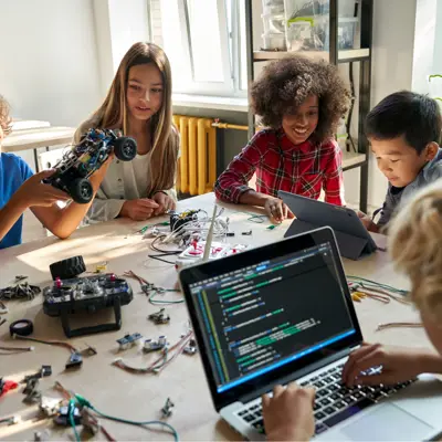 Five children sitting around a table coding and building a toy car.