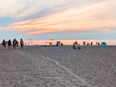 Orange and blue skies over a sandy beach with beachgoers scattered along the shore.