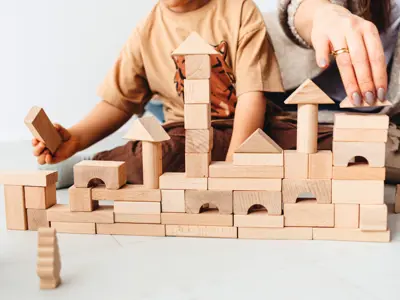 A child and an adult building a castle from wooden blocks.