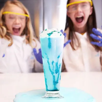 Two girls smiling and conducting a science experiment creating a blue potion.