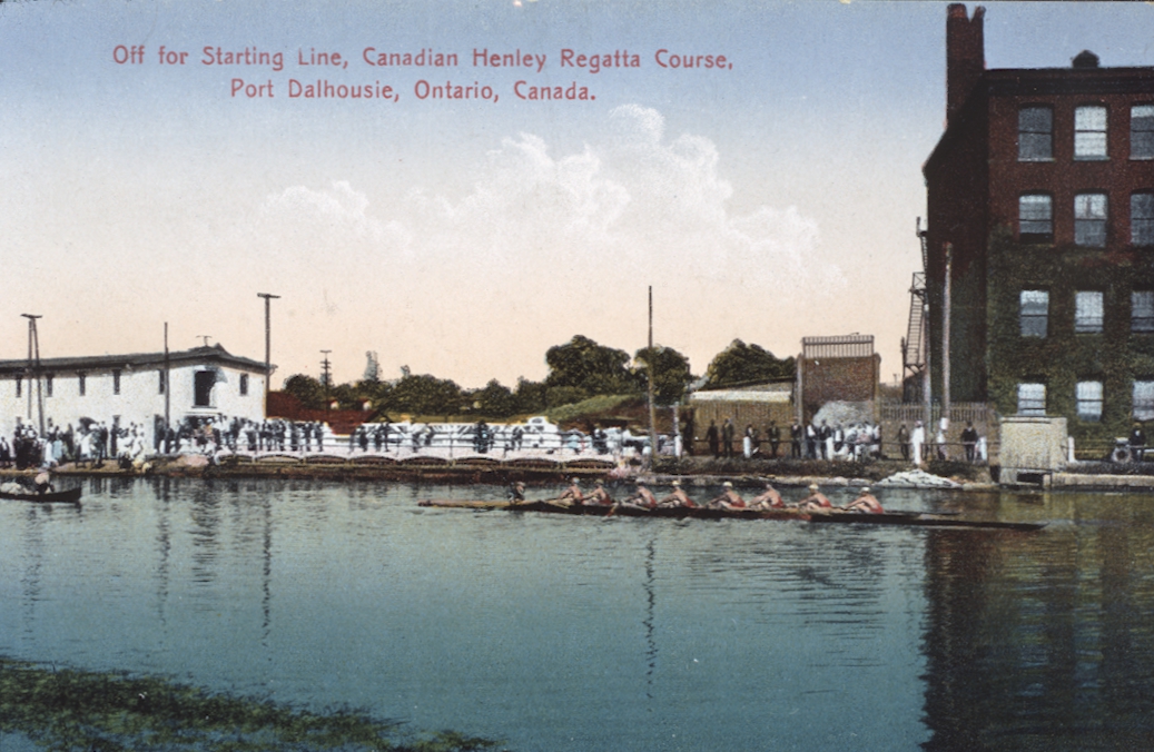 A vintage post card of a rowing boat in a pond at the starting line of the Royal Canadian Henley Regatta.