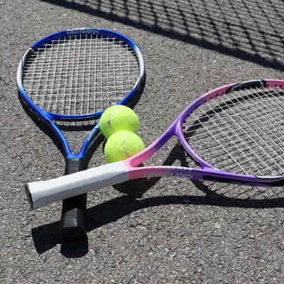 Two tennis rackets and two tennis balls laying on the pavement.