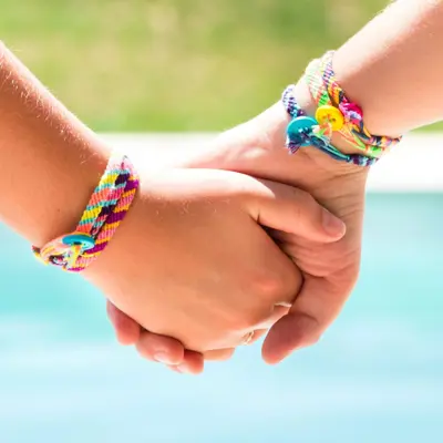 Hands holding one another, each with several colourful bracelets on their wrists.