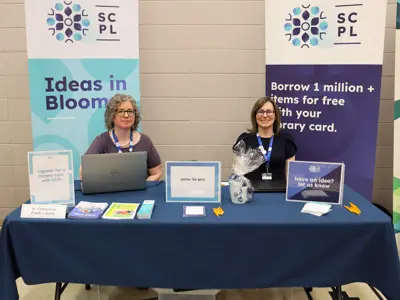 Two library staff members sit at an information table.