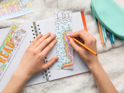 Hands colouring in a bookmark using pencil crayons.
