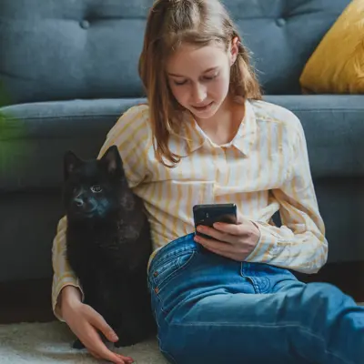 A girls sits on the floor with her dog while scrolling on her cell phone.