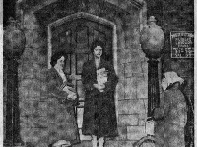A black and white newspaper photo of three young women holding books and standing on the front steps on the Merritton library branch.
