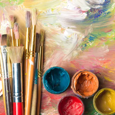Paint brushes and paint pots sitting on a colourful surface.