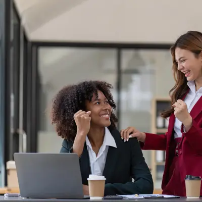 Two women in an office environment celebrating.