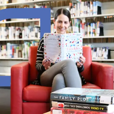 A woman sitting in a red chair in the library reading a book.