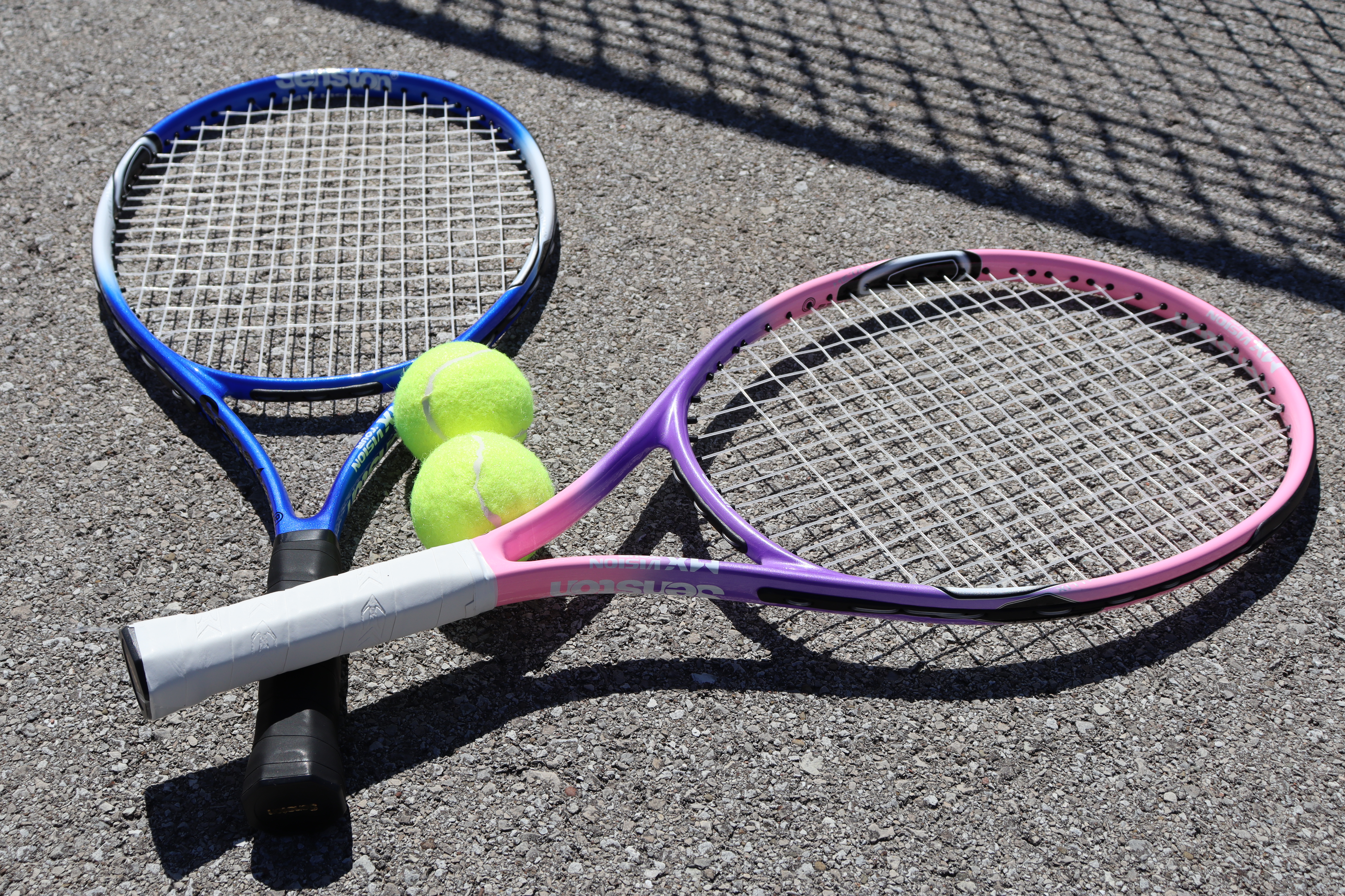 Two tennis rackets and two tennis balls laying on the pavement.