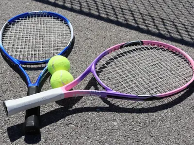 Two tennis rackets and two tennis balls laying on the pavement.