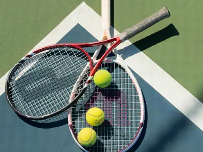 Two tennis rackets and three tennis balls laying a tennis court.