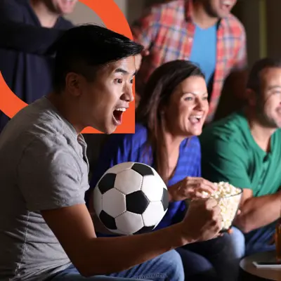 Man holding a soccer ball cheering at a television at a watch party.