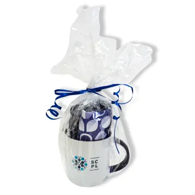 A white mug and rolled up fabric bag bundled up in clear cellophane and blue ribbon.