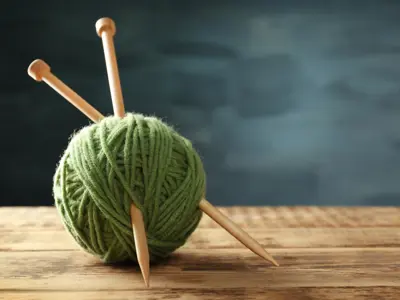 Knitting needles stuck into a sage green ball of yarn.