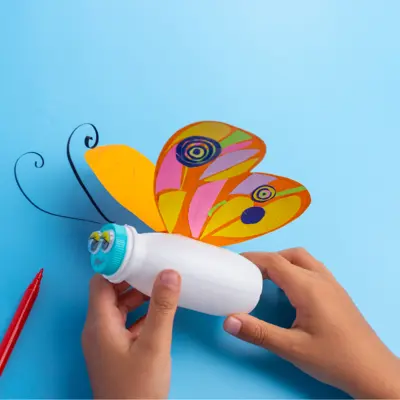 Children's hands holding a butterfly made some crafting supplies.