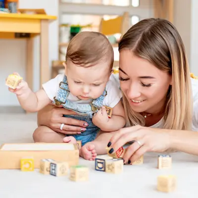 A teen girl playing with blocks with a baby.
