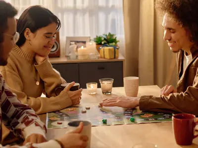Friends gathered around a table playing a board game and smiling.