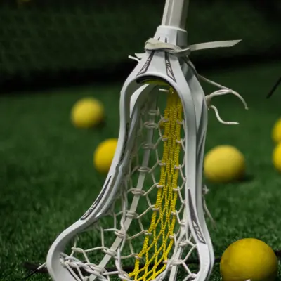 A lacrosse stick propped up on some turf surrounded by lacrosse balls.