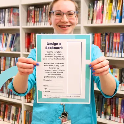 Women in bright blue shirt holding up the Library's Design a Bookmark Contest entry ballot.