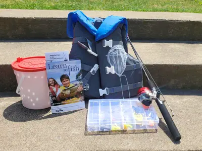 A life vest, fishing rod, tackle box, bucket, and instructional booklet sitting on concrete steps outside.