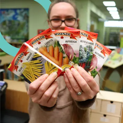 Woman holding out a variety of vegetable seed packets towards the camera.