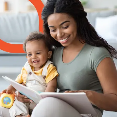 A Black woman reads a book to a baby sitting in her lap.