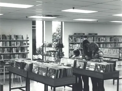 A black and white photo of three young girls sorting through vinyl records at the library in 1966.