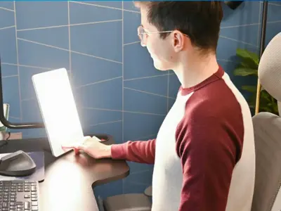 Man sitting as computer desk with a therapy lamp.