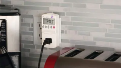 A Kill a Watt device plugged into a kitchen wall outlet.