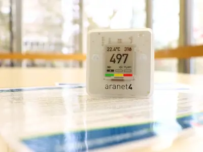 White carbon dioxide detector with digital screen sitting with instructional pamphlet on a library table.