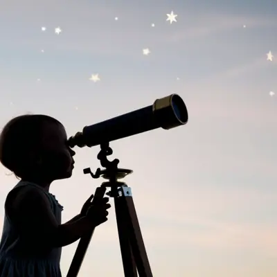 The silhouette of a child looking through a telescope into the night sky.