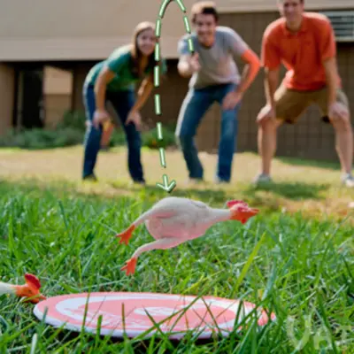 From the background, three people play Flickin' Chicken by throwing a rubber chicken toy towards a target on the ground.