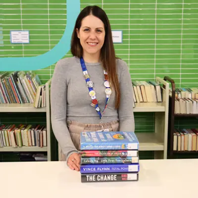 A librarian stands are a service counter with a stack of books.