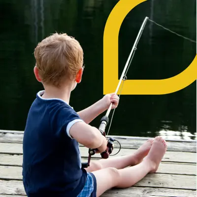 A child sitting on a dock and facing the water holding a fishing rod.