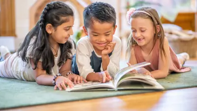 Three childing laying on the floor reading a book together/
