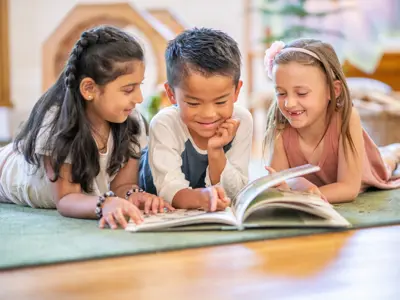 Three childing laying on the floor reading a book together/