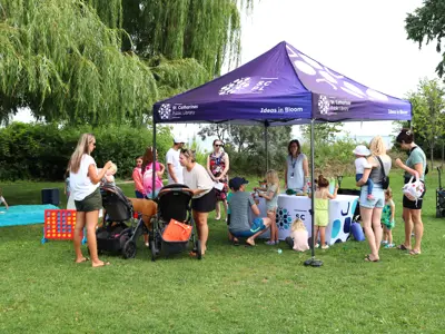 Community members gather around a library tent and table at the park.