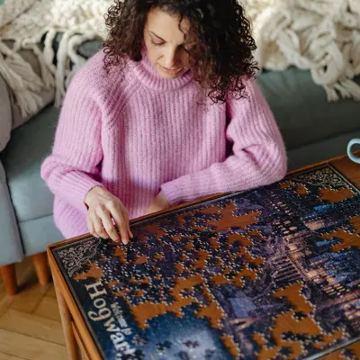 A woman in a bright pink sweater assembling a jigsaw puzzle.