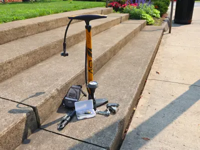 A bike tire pump, wrenches, and various other small tools sitting on concrete steps outside.