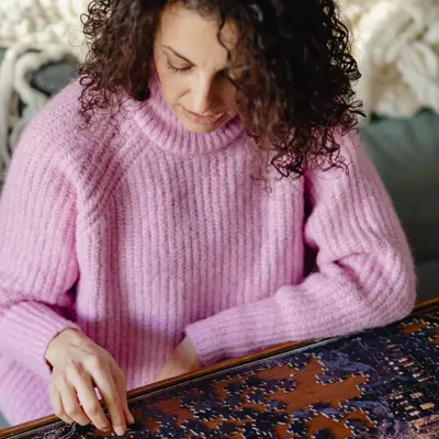 A woman in a pink sweater building a jigsaw puzzle.