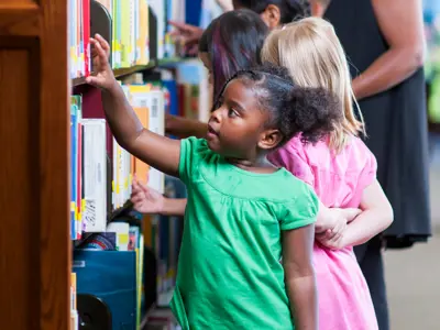 A young girl looking through the books on the shelf at a library.